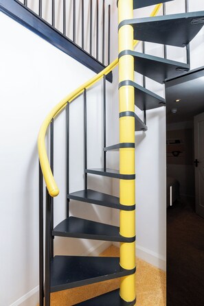 A spiral staircase with black steps and yellow handrails. - Kirkstone Pass Mountain Rooms (Windermere)