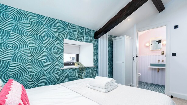 Un dormitorio con cama, ventana, baño con lavabo y espejo, y pared con diseño.
