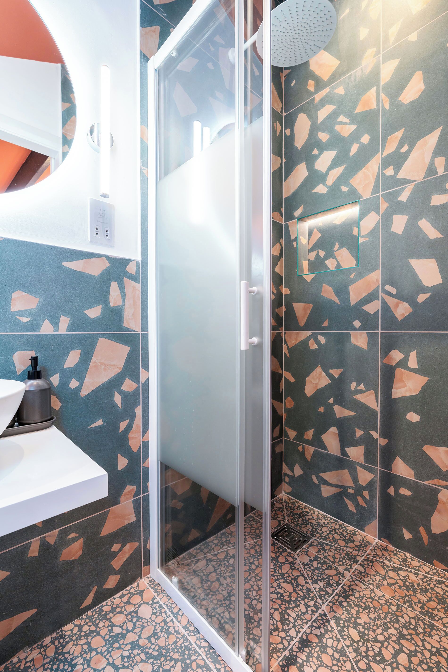A modern bathroom with a glass shower enclosure, a sink with a soap dispenser, and a wall with a geometric tile pattern.