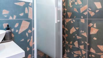 A modern bathroom with a glass shower enclosure, a sink with a soap dispenser, and a wall with a geometric tile pattern.