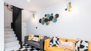 Un salon moderne avec un sol à carreaux, un canapé gris agrémenté de coussins jaunes et un escalier noir.