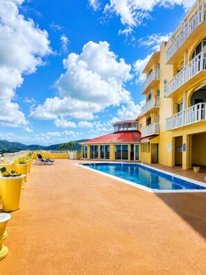 A rooftop pool area with a red-roofed structure, yellow buildings, and a clear blue sky. - Welcome to Island Breeze, Your Oceanfront Escape in Beautiful St. Croix (Christiansted)