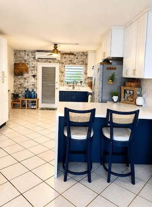 A kitchen with a stone backsplash, white cabinets, and a bar area with two chairs. - Welcome to Island Breeze, Your Oceanfront Escape in Beautiful St. Croix (Christiansted)