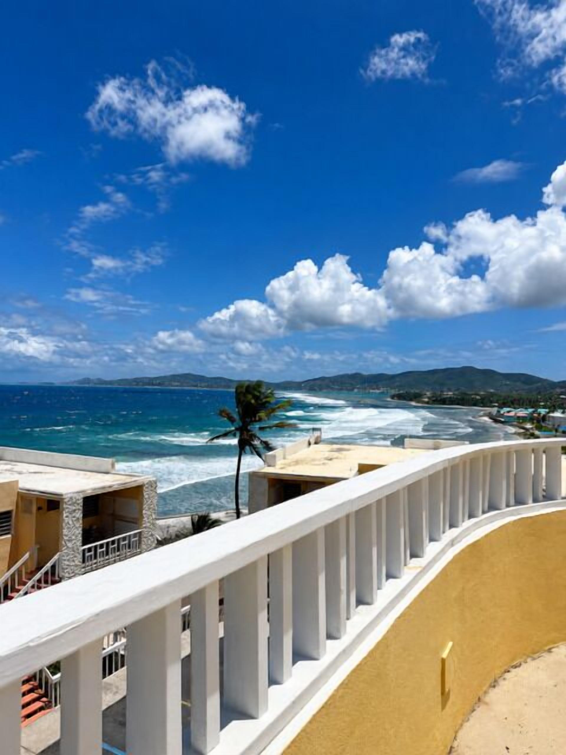 A coastal view with a white balcony railing, ocean waves, and distant mountains.