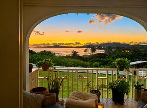 A balcony with a view of a sunset over a landscape, including a fence and potted plants. - Welcome to Island Breeze, Your Oceanfront Escape in Beautiful St. Croix (Christiansted)