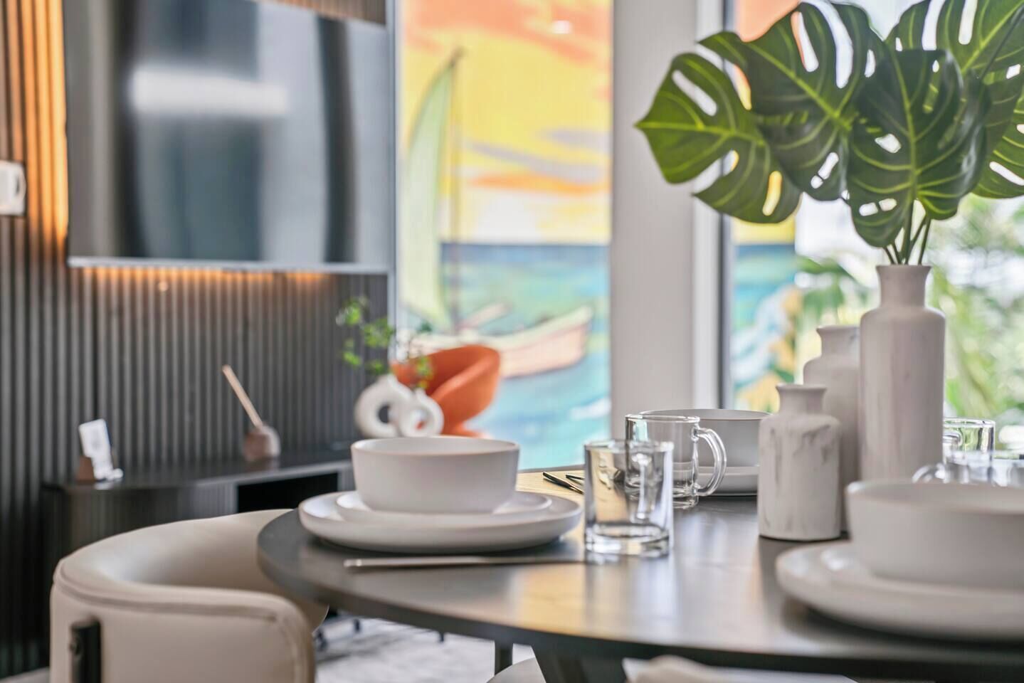 Un comedor con una mesa redonda preparada para dos personas, con platos, tazones y vasos blancos.