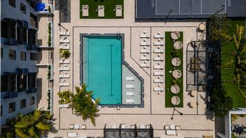A rooftop pool area with sun loungers, a tennis court, and a landscaped garden.