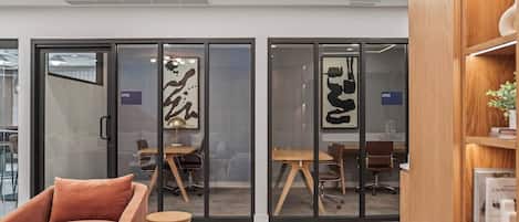 Un espace de bureau avec des cloisons en verre, un bureau en bois, des chaises de bureau et une bibliothèque.