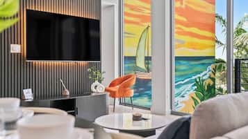 Een moderne woonkamer met een flatscreen televisie, een ronde salontafel en een kleurrijke muurschildering van een zonsondergang.