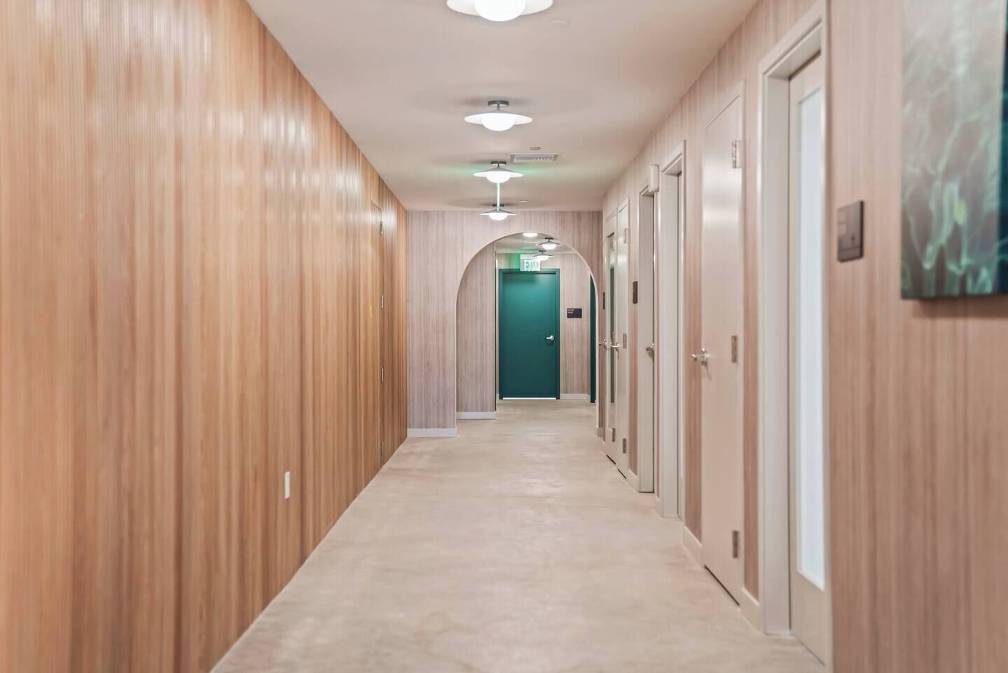 A hotel hallway with wooden paneling, a carpeted floor, and a green exit door at the end.