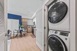 A laundry room with stacked washers and dryers, a dining area with a table and chairs, and a kitchen with cabinets and appliances. - 5 Mins to Beach | Pickle ball | Resprt Style Pool | Free Parking (Fort Lauderdale)