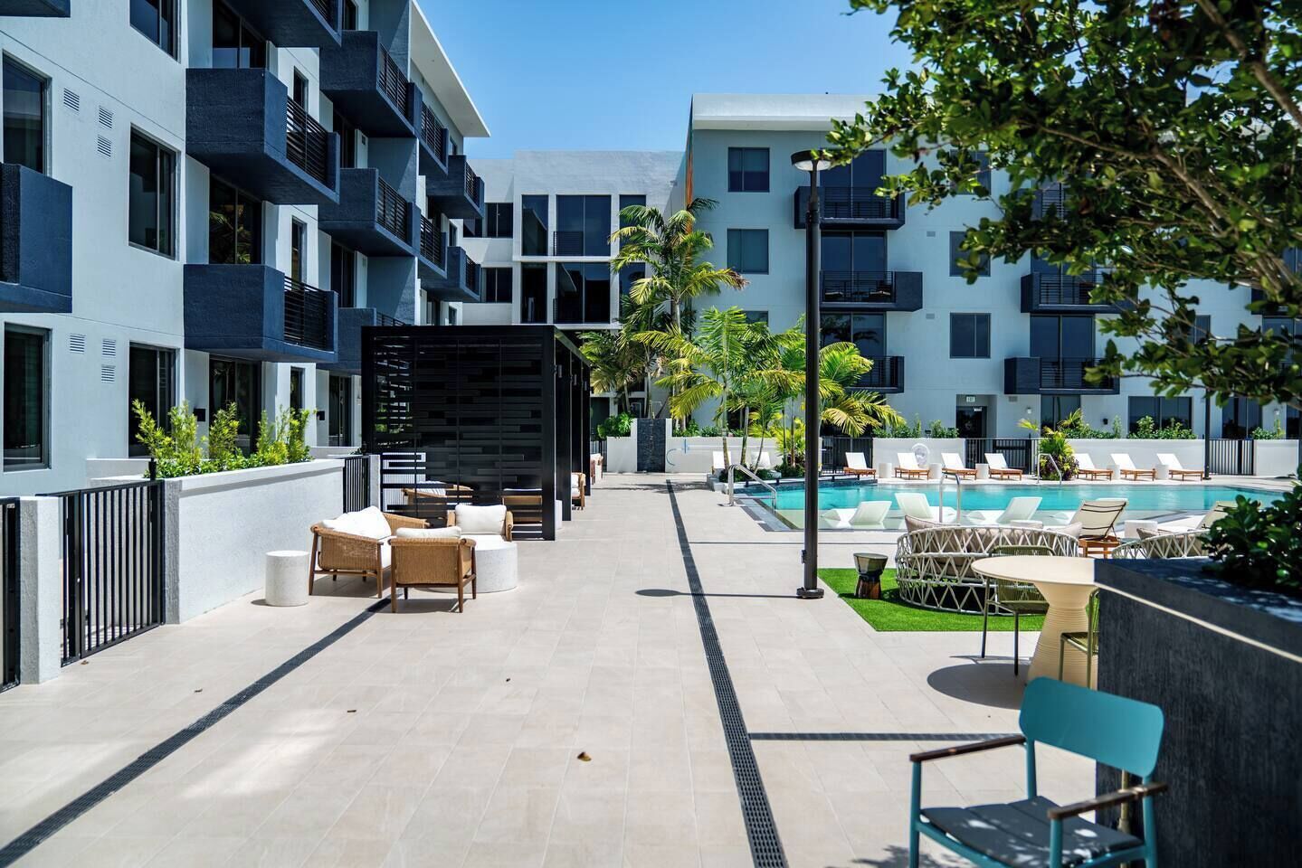 A modern outdoor pool area with lounge chairs and a seating area, surrounded by multi-story buildings with balconies.