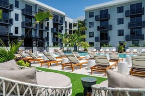 A poolside area with lounge chairs and a swimming pool, surrounded by a building with balconies.