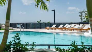 A swimming pool with lounge chairs and a fence, surrounded by greenery.
