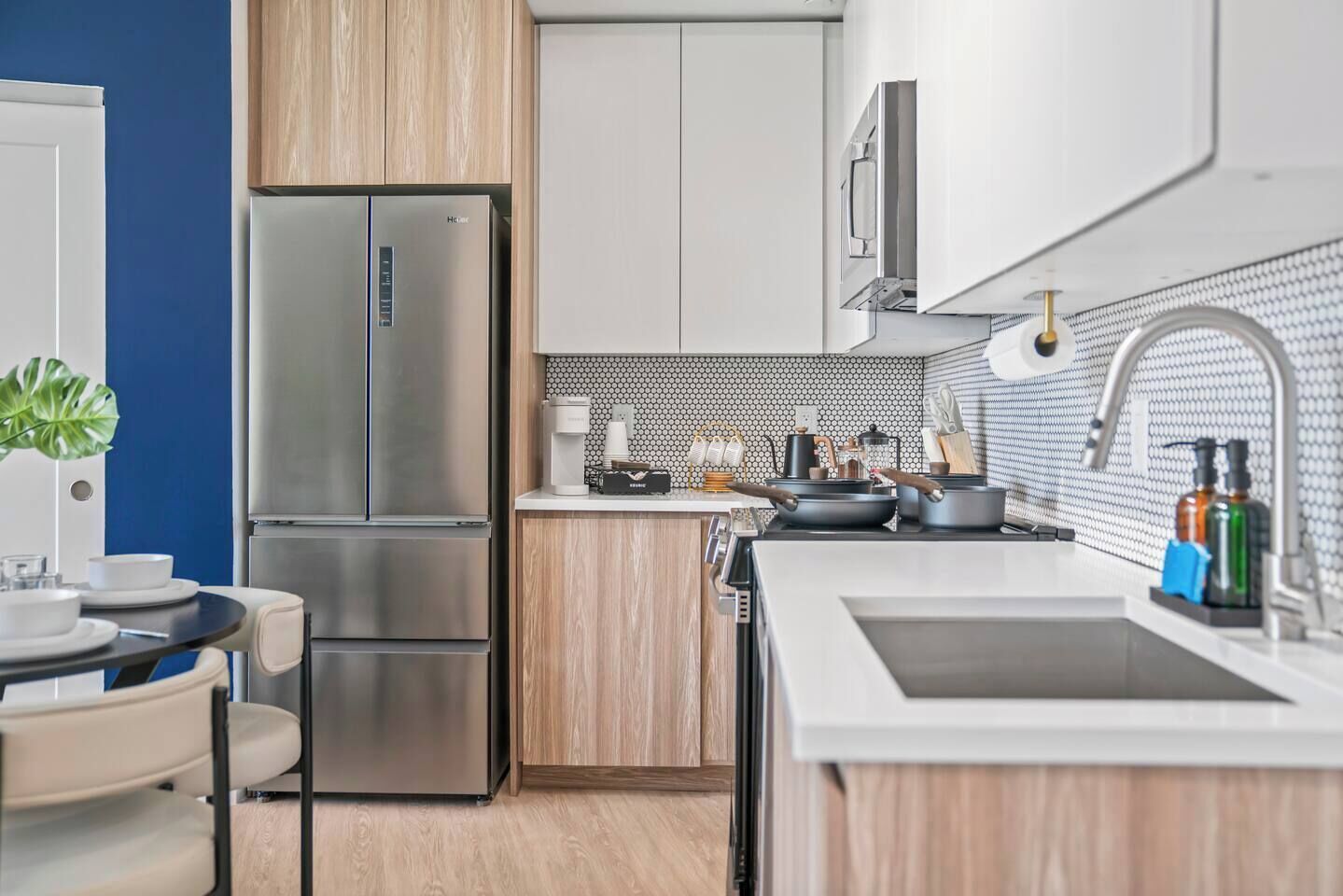 A modern kitchen with a stainless steel refrigerator, wooden cabinets, a white countertop, and a sink with a faucet.