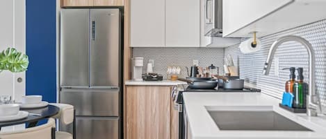 A modern kitchen with a stainless steel refrigerator, wooden cabinets, a white countertop, and a sink with a faucet.