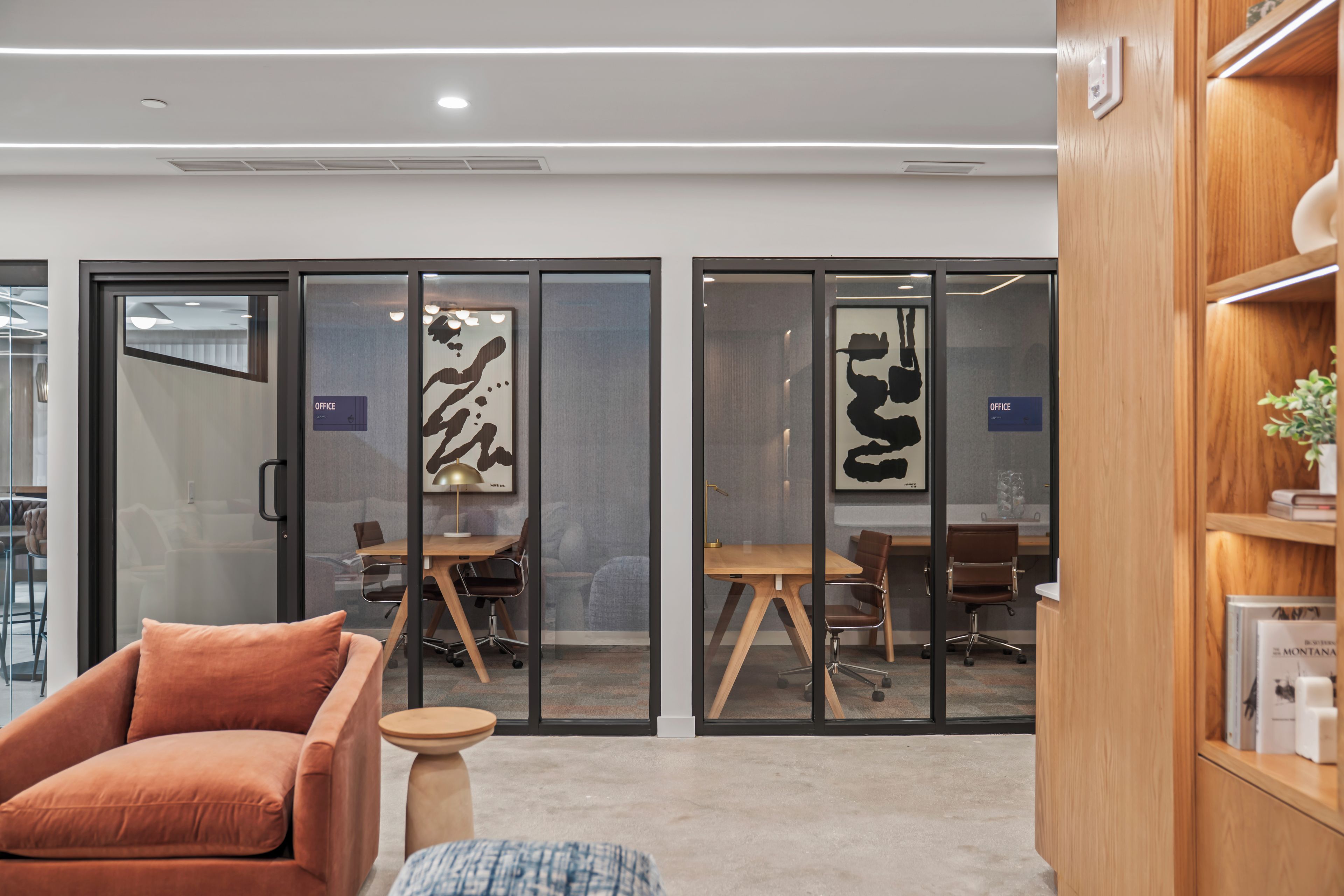An office space with glass partitions, a wooden desk, a brown chair, and a small round table.