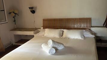 Une chambre d’hôtel avec un grand lit, deux serviettes roulées, une tête de lit en bois, une table de chevet ornée d’un vase de fleurs et une lampe fixée au mur.