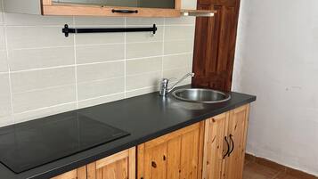 Une cuisine avec des meubles de rangement en bois, un plan de travail noir, un évier en acier inoxydable et une porte en bois.