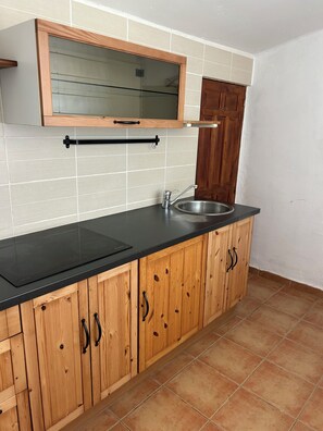 A kitchen with wooden cabinets, a black countertop, a stainless steel sink, and a wooden door.