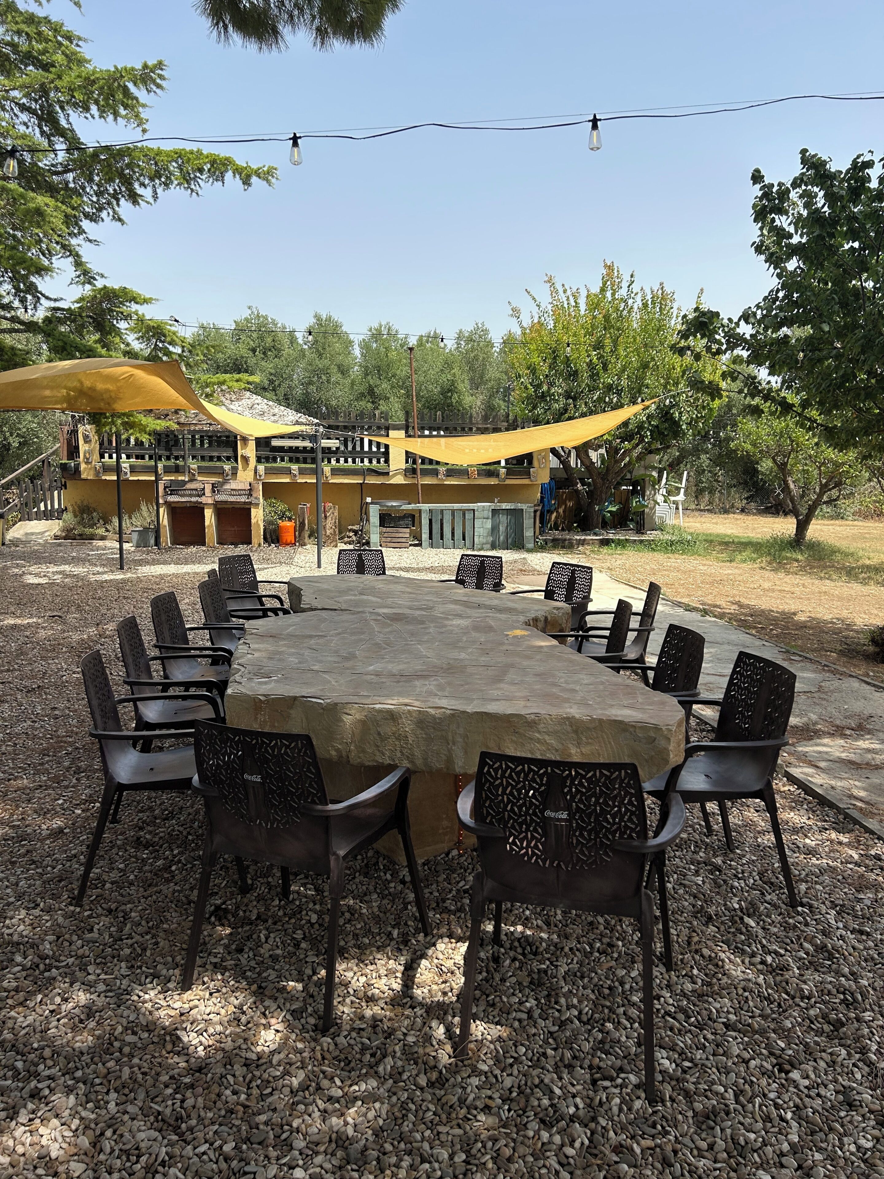 An outdoor dining area with a stone table and black chairs, surrounded by gravel.
