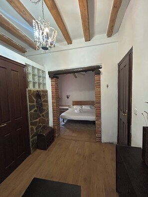 A room with a bed, a stone wall, a wooden floor, and a chandelier.