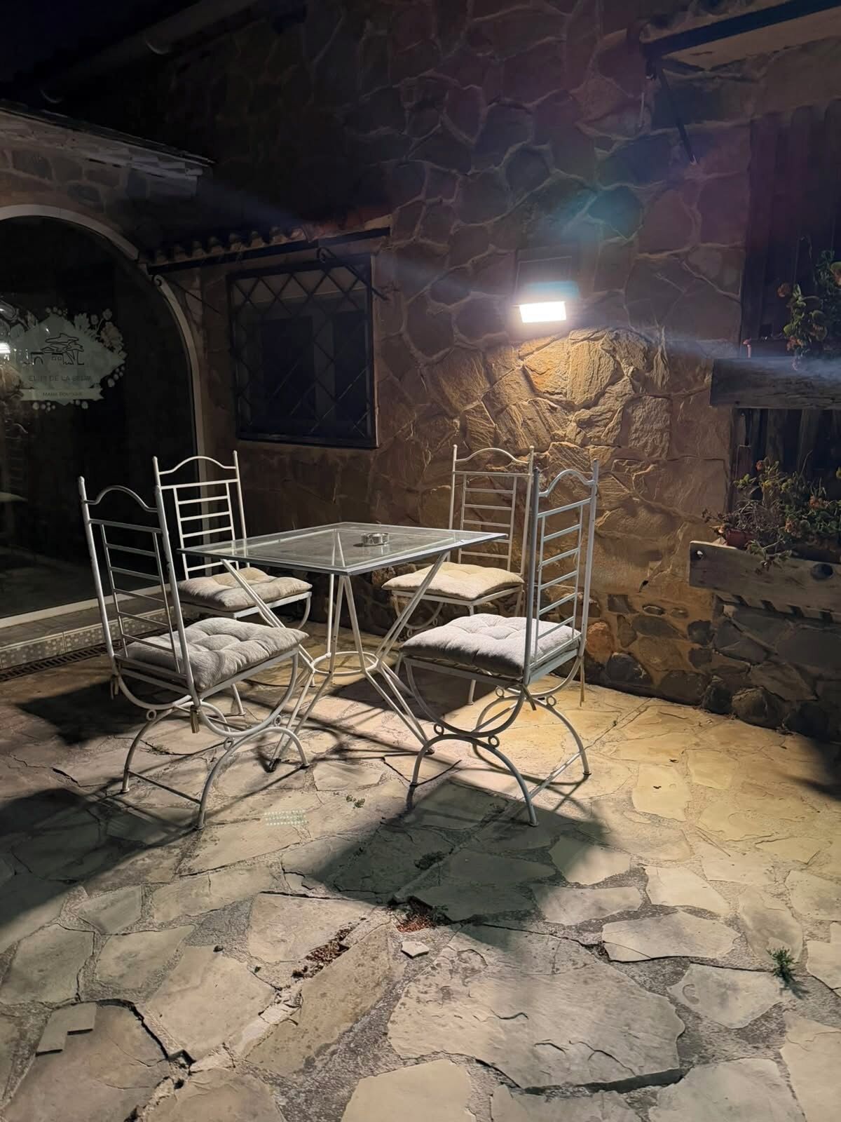 An outdoor dining area with a stone wall and metal chairs.