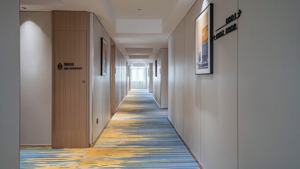 A hotel hallway with a patterned carpet, wooden doors, and framed pictures on the walls. - Poltton International Apartment (Zhanjiang Xuwen Chengdong Dadao) (Zhanjiang)