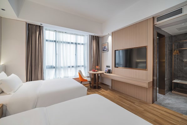 Habitación de hotel con dos camas, televisión, una mesita con una silla y zona de ducha.