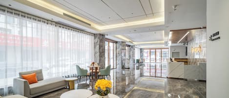 A modern hotel lobby with a sofa, round tables, and a reception desk.
