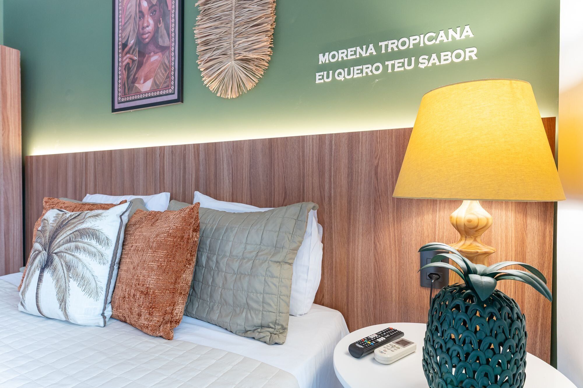 Habitación de hotel con cama, almohadas, una obra de arte colgada en la pared, un adorno decorativo, una lámpara y un control remoto sobre una mesita de noche.