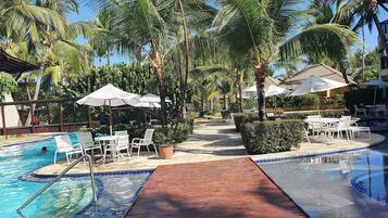 A pool area with lounge chairs and umbrellas, surrounded by palm trees and a clear sky.