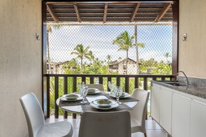 A balcony with a table set for two, chairs, a sink, and a view of palm trees and buildings. - Nannai Residence Frente Piscina (Ipojuca)