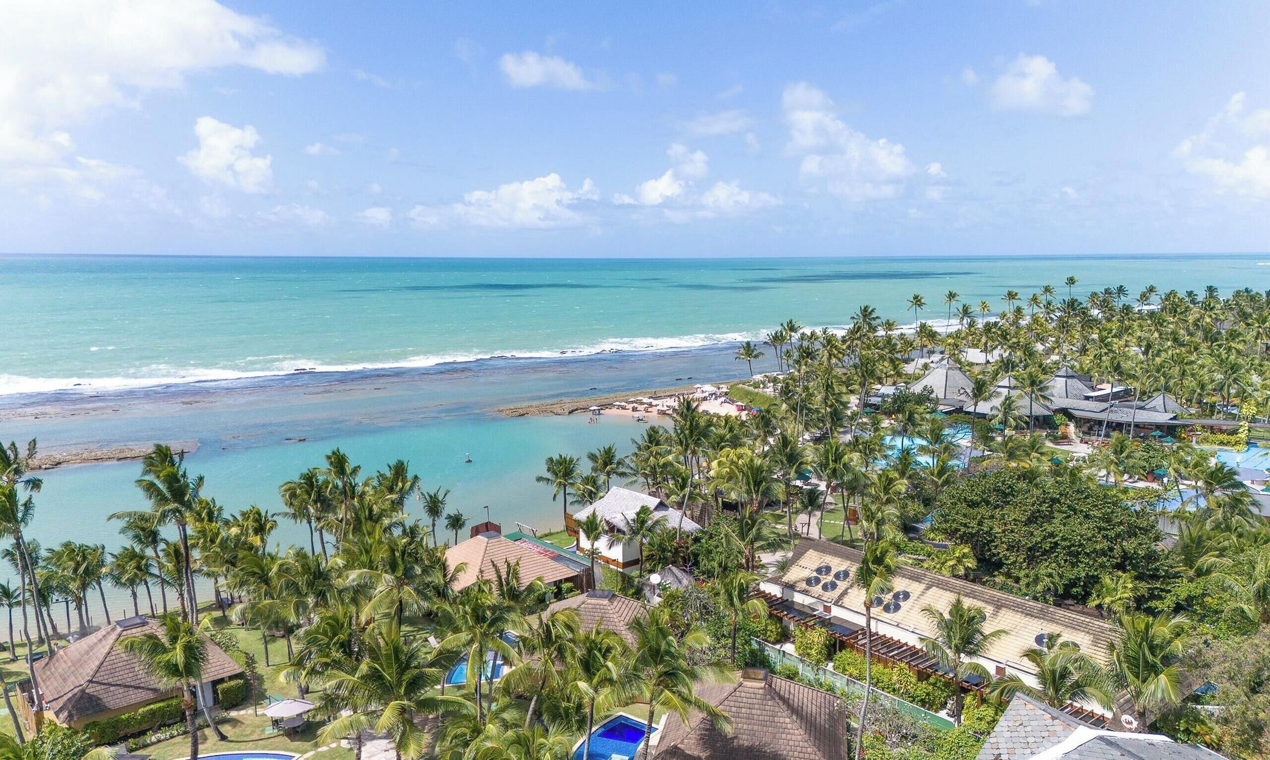 Resort com vista para a praia, várias piscinas e céu claro.