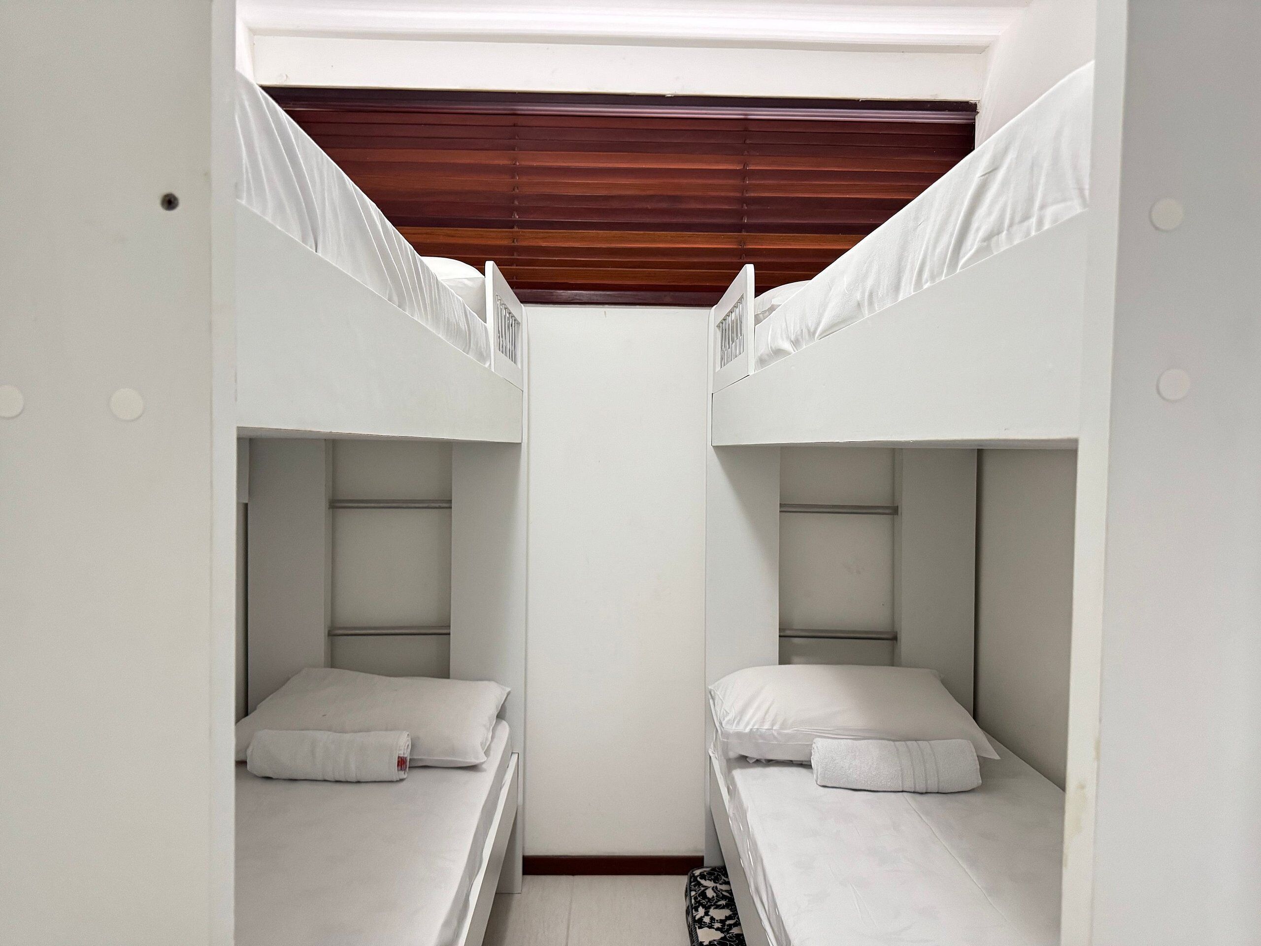 Habitación con literas, ropa de cama blanca y techo de madera.
