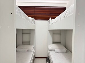 Een slaapkamer met stapelbed, witte beddengoed en een houten plafond.