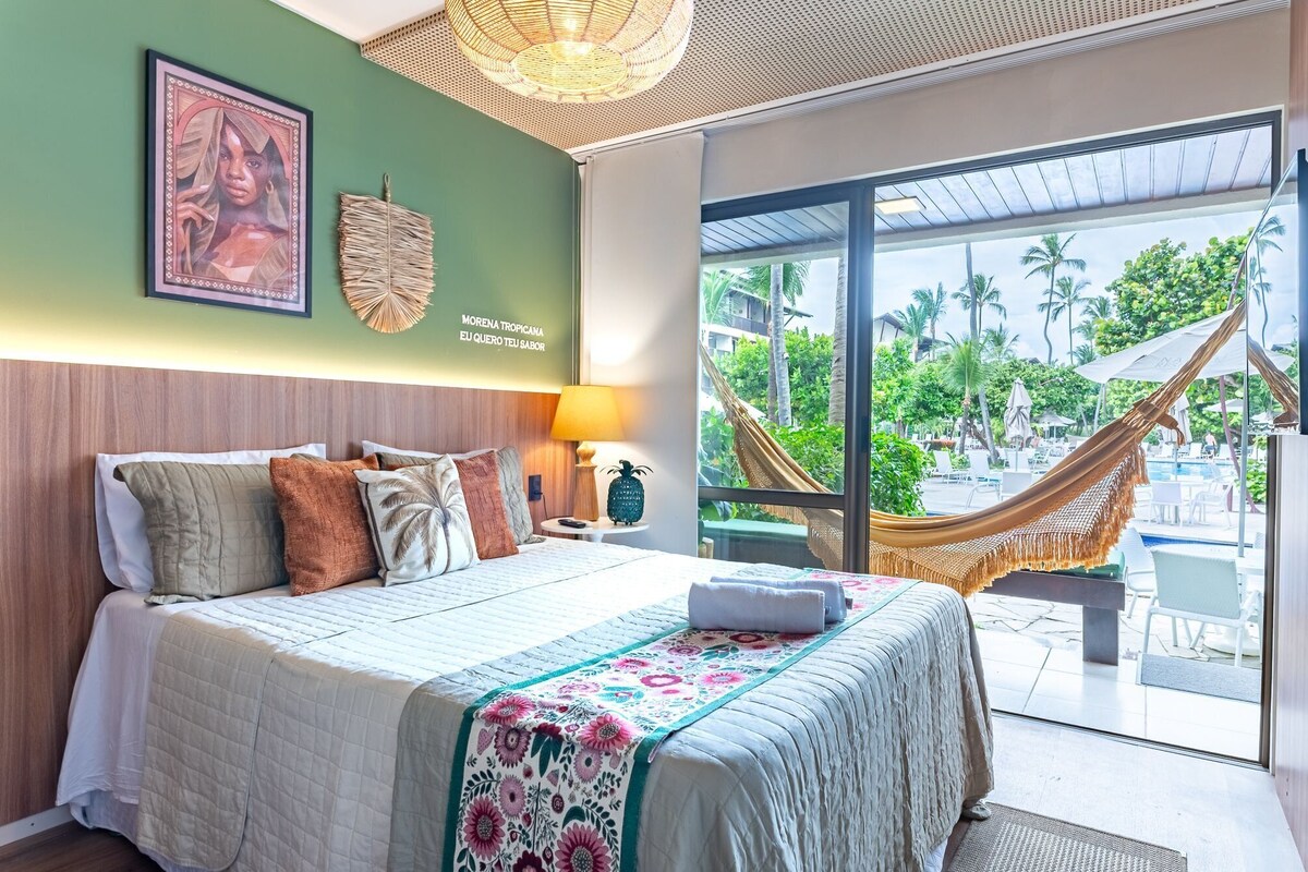 Ein Hotelzimmer mit Bett, einer Hängematte, Blick auf einen Pool und einer Wanddekoration im tropischen Stil.