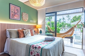 Ein Hotelzimmer mit Bett, einer Hängematte, Blick auf einen Pool und einer Wanddekoration im tropischen Stil.