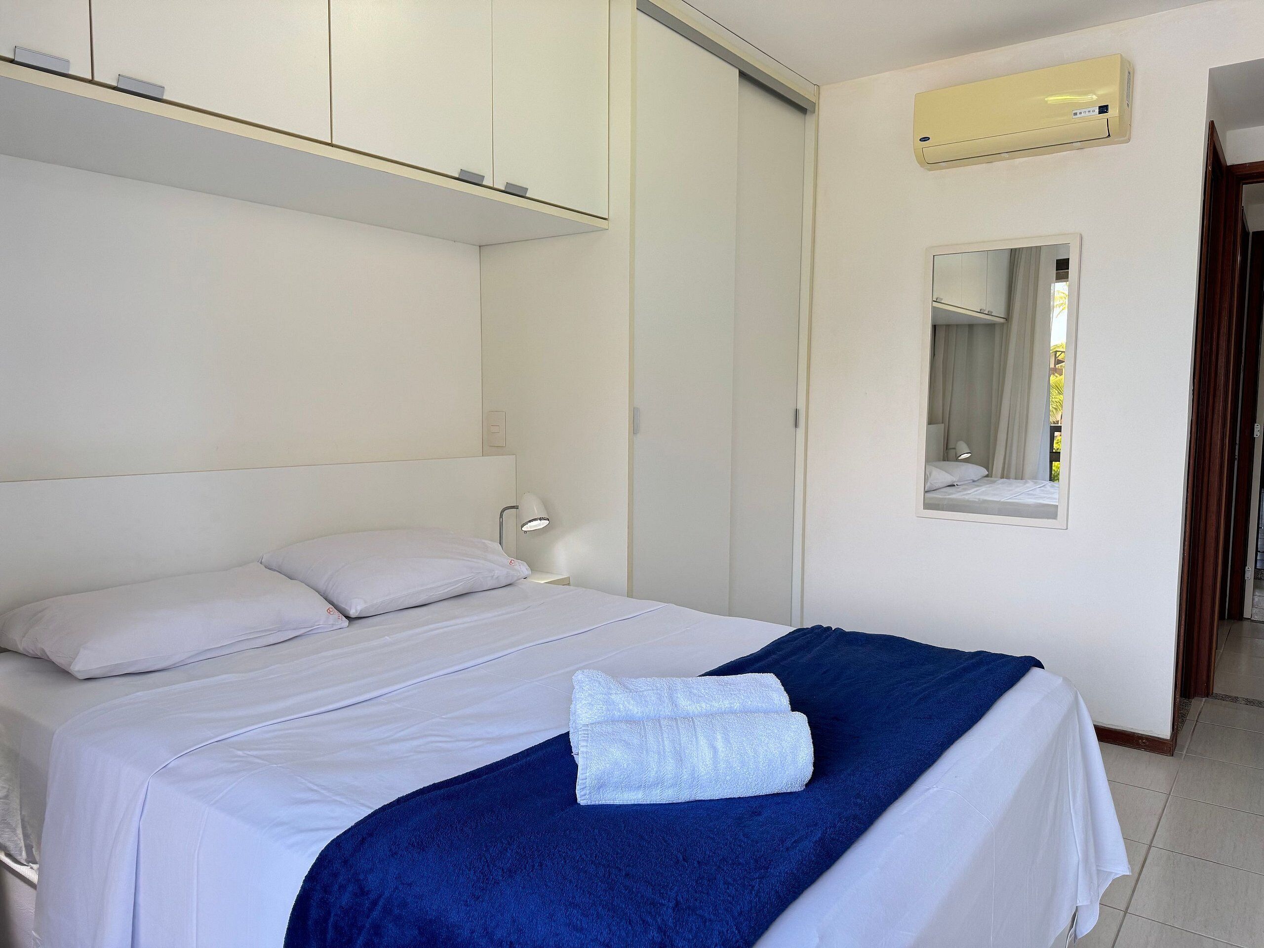 Quarto de hotel com cama, abajur, espelho e ar condicionado.