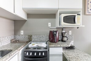 Una kitchenette equipada con estufa a gas, microondas, cafetera y un lavamanos pequeño.