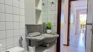 A bathroom with a white toilet, a sink with a granite countertop, a mirror, and a shower area.
