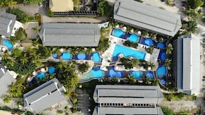 An aerial view of a resort with multiple swimming pools, palm trees, and a parking area.