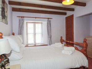 A bedroom with a large bed, wooden headboard, a window with curtains, and a wooden door. - Honeysuckle (Newquay)
