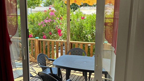A wooden deck with a table and chairs, an umbrella, and a view of a garden with pink flowers. - Le Cabanon des Étangs by Sur la mer (Fréjus)