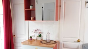 A room with a white wardrobe, a mirror above it, a small table with a plant, and a red curtain. - Le Cabanon des Étangs by Sur la mer (Fréjus)