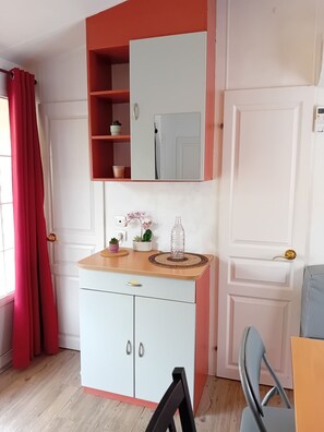 Ein Zimmer mit einem weißen Kleiderschrank, einem Spiegel darüber, einem kleinen Tisch mit einer Pflanze und einem roten Vorhang.