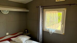 A bedroom with a bed, a bedside table, a lamp, a window with a curtain, and a wall-mounted picture. - Le Cabanon des Étangs by Sur la mer (Fréjus)