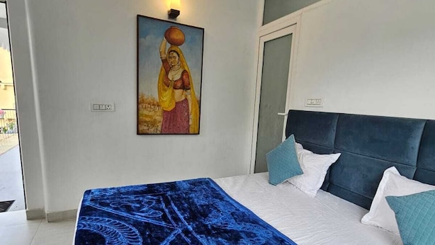 A bedroom with a bed, a ceiling fan, a painting on the wall, and a door. - Sukon House by Crimson Horizon (Mussoorie)