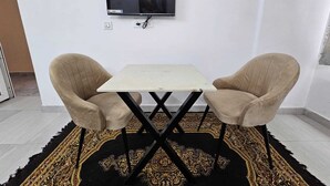 A room with a television mounted on the wall, a small table with two chairs, and a patterned rug on the floor. - Sukon House by Crimson Horizon (Mussoorie)