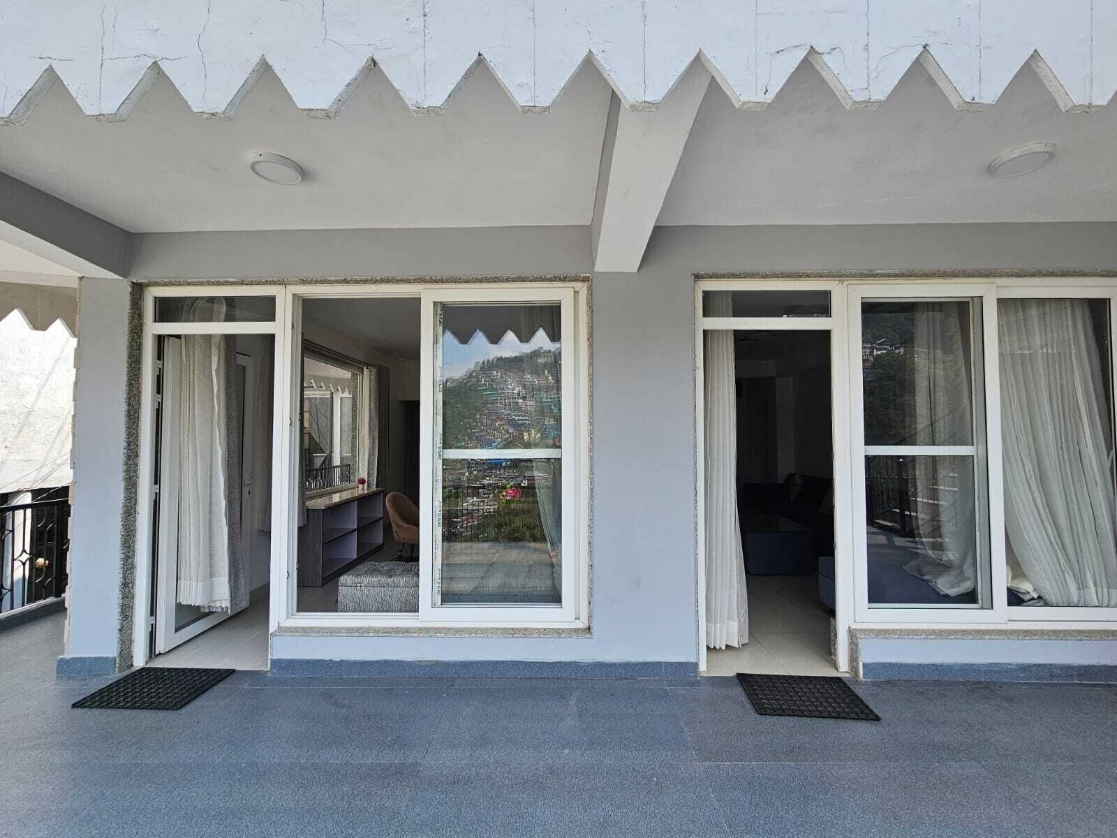 Un edificio con dos puertas correderas de vidrio abiertas que dan a balcones, uno con vista a un paisaje montañoso y otro a una zona residencial.